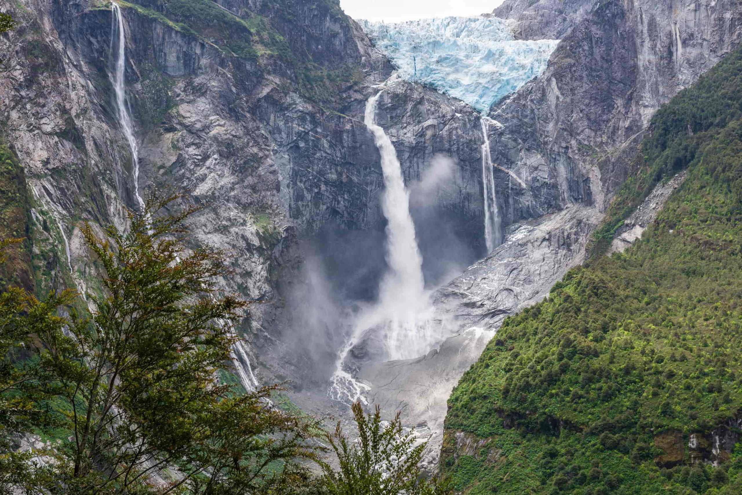 Hanging glacier and meltwater waterfalls between rock walls and native forest
